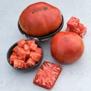 A couple of whole German Pink Tomatoes with chopped and cut tomatoes  on light background.