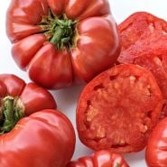 Close-up of cut and whole German Pink tomatoes on a white background.