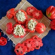 Stuffed Gezahnte Tomatoes with slices arranged on bamboo matt on a royal blue background.