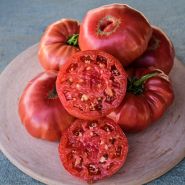 Cut and whole Granny Cantrell German Red Tomatoes on a terra-cotta red pizza stone.