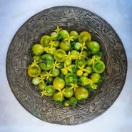 An antique platter full of Green Doctors Tomatoes with blooms on a pale blue background.