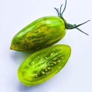 A macro close-up of a whole Greentiger Tomato with a half slice on a white background.