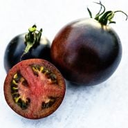 A trio of Indigo Blue Chocolate Tomatoes with one sliced in half to show the red meat inside.