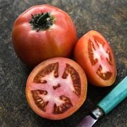 Cut and whole Ozark Pink Tomatoes with a vintage wood handled knife on wooden cutting board.