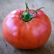 A close-up of a single Ozark Pink Tomato on wood.