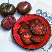 Sliced Paul Robeson Tomatoes on red plate with a Soviet newspaper.