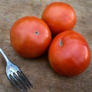 Three whole Peron Tomatoes with an old tarnished fork on wood cutting board.