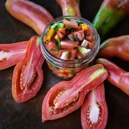 Close-up of cut and whole Pink Fang Tomatoes with salsa in a jar on a copper background.