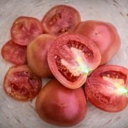 Cut and whole Raspberry Lyanna Tomatoes on a pink terra-cotta plate.