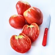 Whole and cut Hungarian Heart Tomatoes on white background with a red handled knife.