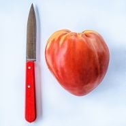An Hungarian Heart Tomato on a white background with a red handled knife to show its size.