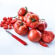 A bounty of chopped, cut and whole Millionaire Tomatoes with a red handled peeler on white background.