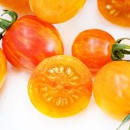 Close-up macro view of sliced and whole Sunrise Bumble Bee Tomatoes on a white background.