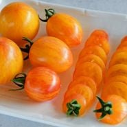 Whole and sliced Sunrise Bumble Bee Tomatoes on a white plate.