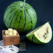 A whole Silver Yamato Watermelon with a quarter slice and melon balls in a wooden Japanese box on a jade background.