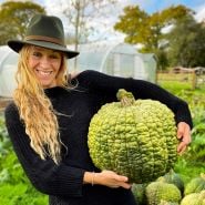 A smiling woman holding a Crespo Winter Squash in her garden. Image Courtesy of Lucy Hutchins.