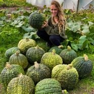A smiling woman sits by a productive Crespo Winter Squash harvest. Image Courtesy of Lucy Hutchins.