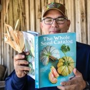 A smiling Baker Creek manager reading the 2025 Whole Seed Catalog while holding corn that he grew.