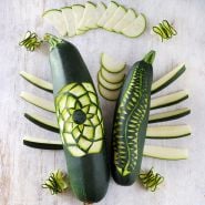 Black Beauty Zucchini Summer Squash carved and sliced on a white washed wood background.