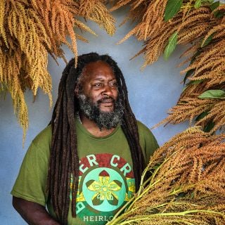 A Baker Creek horticulturalist poses with Golden Giant Amaranth stalks in Baker Creek shirt.