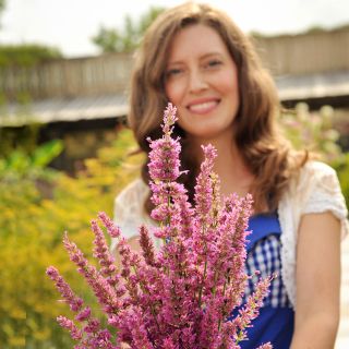 A woman holding a bouquet of Arcado Pink Agastache in the trial garden in front of the Baker Creek Seed Store.