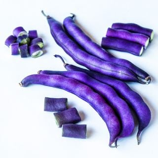 Cut and whole Purple Dove Bush Beans arranged on a white background.