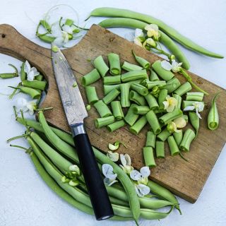 Chopped Contender Beans on a cutting board with a knife surrounded by whole beans on white.