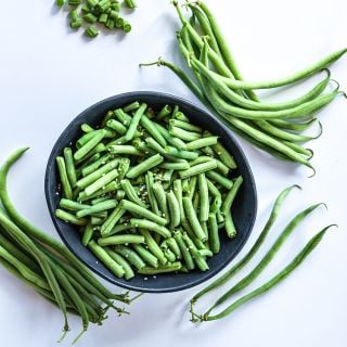 Cutand cooked Calima Beans in bowl surrounded by whole beans on a white background.