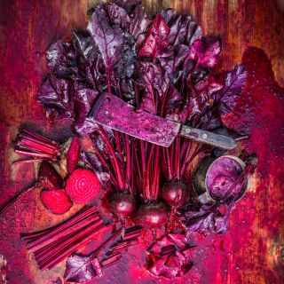 Overhead view of gory Bull's Blood Beets scene with a rusty butcher's knife covered in beet juice.