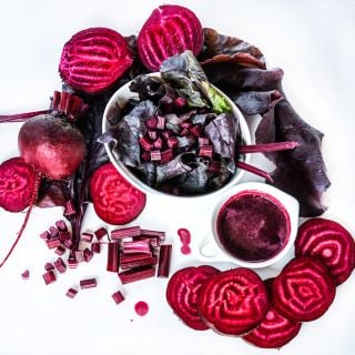 A salad made from beet greens surrounded by sliced Bull's Blood Beets and juice on a white background.