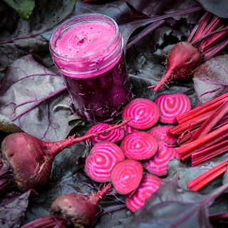 A mason jar full of Bull's Blood Beet juice on abed of red leaves with sliced and whole beets.