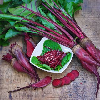 Sliced and whole Renova Beets with foliage and beet salad in bowl on a wooden background.