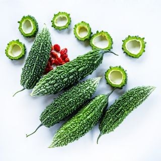 Whole and cut Abashi Bitter Melon arranged witht seeds on a white background.