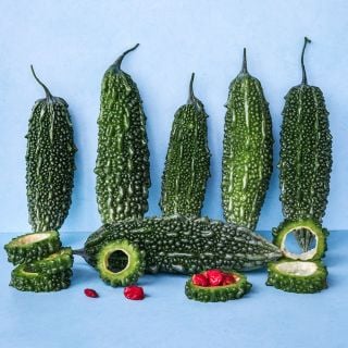 A half dozen Abashi Bitter Melons with slices and seeds on blue background.