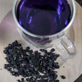 Black Goji Berry (Black Wolfberry) dried on a wooden plate with a cup of Goji berry tea in the background.