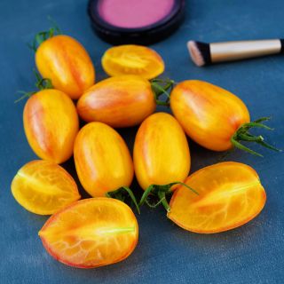 Cut and whole Blush Tiger Tomatoes on a blue background with blush and a make-up brush.