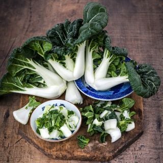 Baby Milk Bok Choy heads on a cutting board with chopped bok choy on a wooden background.