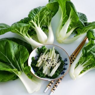 Baby Milk Bok Choy arranged around a bowl of sauteed leaves and stems on a white background.