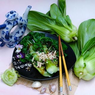 Steamed Suzhou Baby Bok Choy leaves on a plate with fresh heads and vintage Chinese teapot.