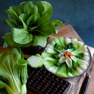 Steamed Suzhou Baby Bok Choy on a plate with fresh bok choy heads on a jade background.