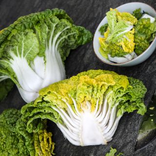 One whole and one half of Yellow Heart Winter Choy heads with leaves in a bowl on a stone background.
