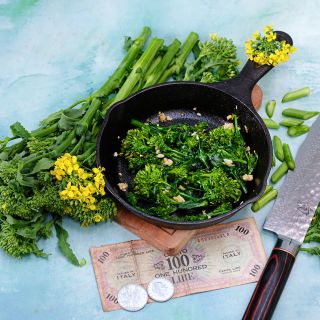 Cooked Natalina Di Fasano Cima Grande Broccoli Rabe in a cast iron skillet surrounded with fresh rabe.