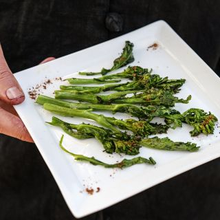 A man holding a grilled plate of gourmet Rapini.
