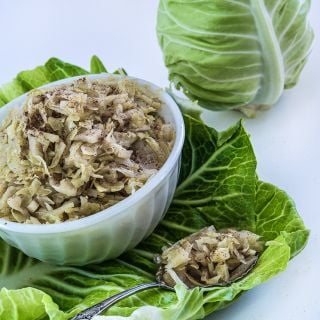 A bowl full of Sauerkraut made from Filderkraut Cabbage rests on a cabbage leaf with spoon.