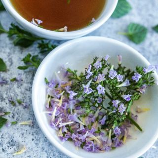 Marvelette Blue Calamintha tea and flowers in white bowls on stone background. 