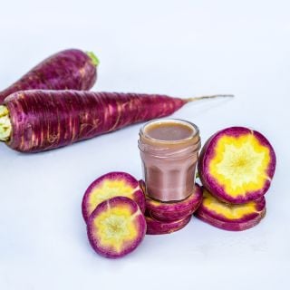 A close-up of Gniff carrot slices with juice and whole carrots in the background.