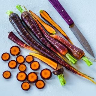 Sliced, cut and whole Lila Lu Sang Carrots with a purple handled knife on a white background.