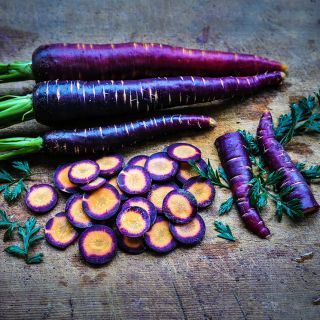 Whole and sliced Lila Lu Sang Carrots with foliage on wooden cutting board.