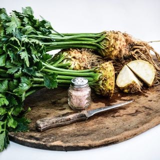Several whole and cut heads of Giant Prague Celeriac with a salt shaker and knife on wooden cutting board.