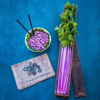 Chinese Pink Celery stalks in wooden box and cut celery in a bowl on a blue background.